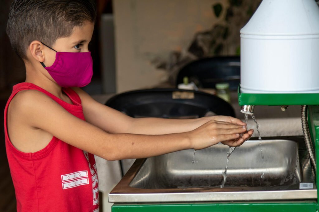 En pojke i Ecuador tvättar händerna. Pojken har en ansiktsmask på sig.