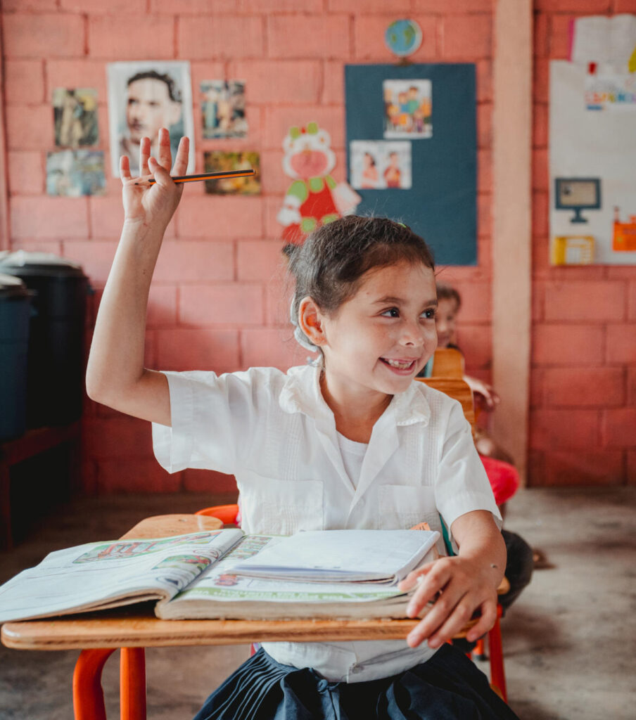 En skolflicka i Honduras sitter i en skolbänk och markerar med handen.