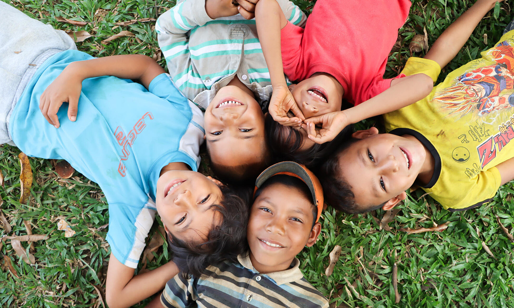 Fem barn från Venezuela ligger på rygg i gräset och ser leende upp mot kameran.