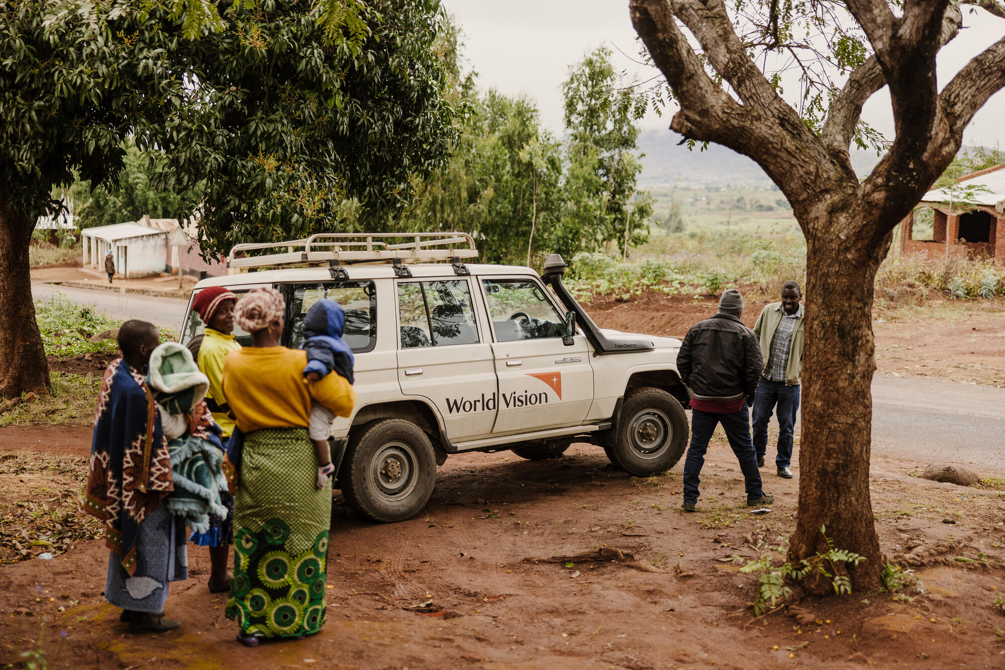 En World Vision Land Rover står parkerad vid sidan av en väg i Malawi. Flera personer står runt bilen.