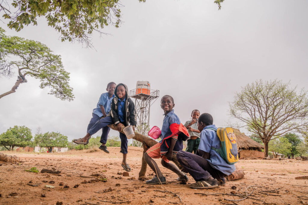 Barn i Zambia gungar tillsammans. I bakgrunden syns ett vattentorn med World Visions logo.